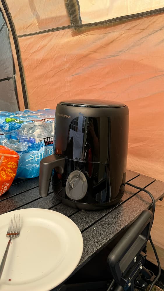 A photo of a small black air fryer sat on a table inside a tent