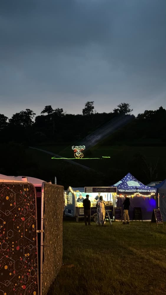 A photo of a hillside at night seen above some food stalls. Projected onto the hillside using lasers is the game &quot;Duck Hunt&quot;