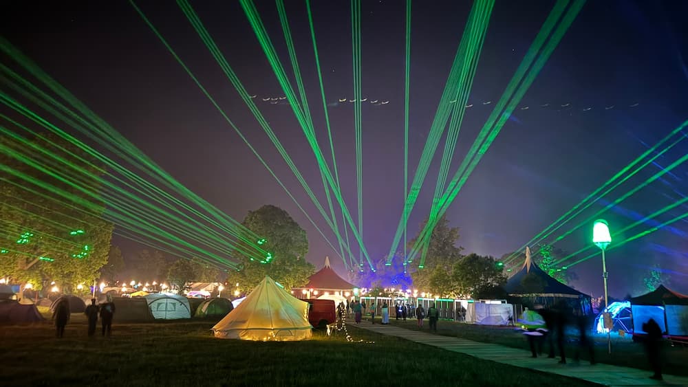 A photo of a campsite with some tents at night with several green lasers being shot into the sky